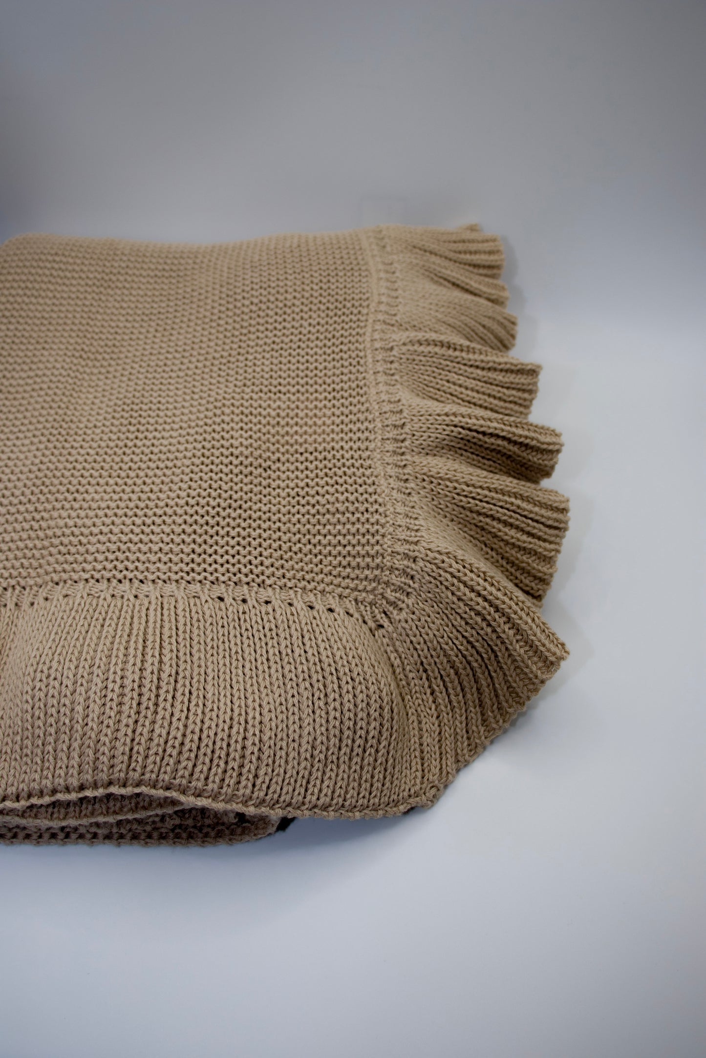Beige knitted blanket with frayed edge on a white background