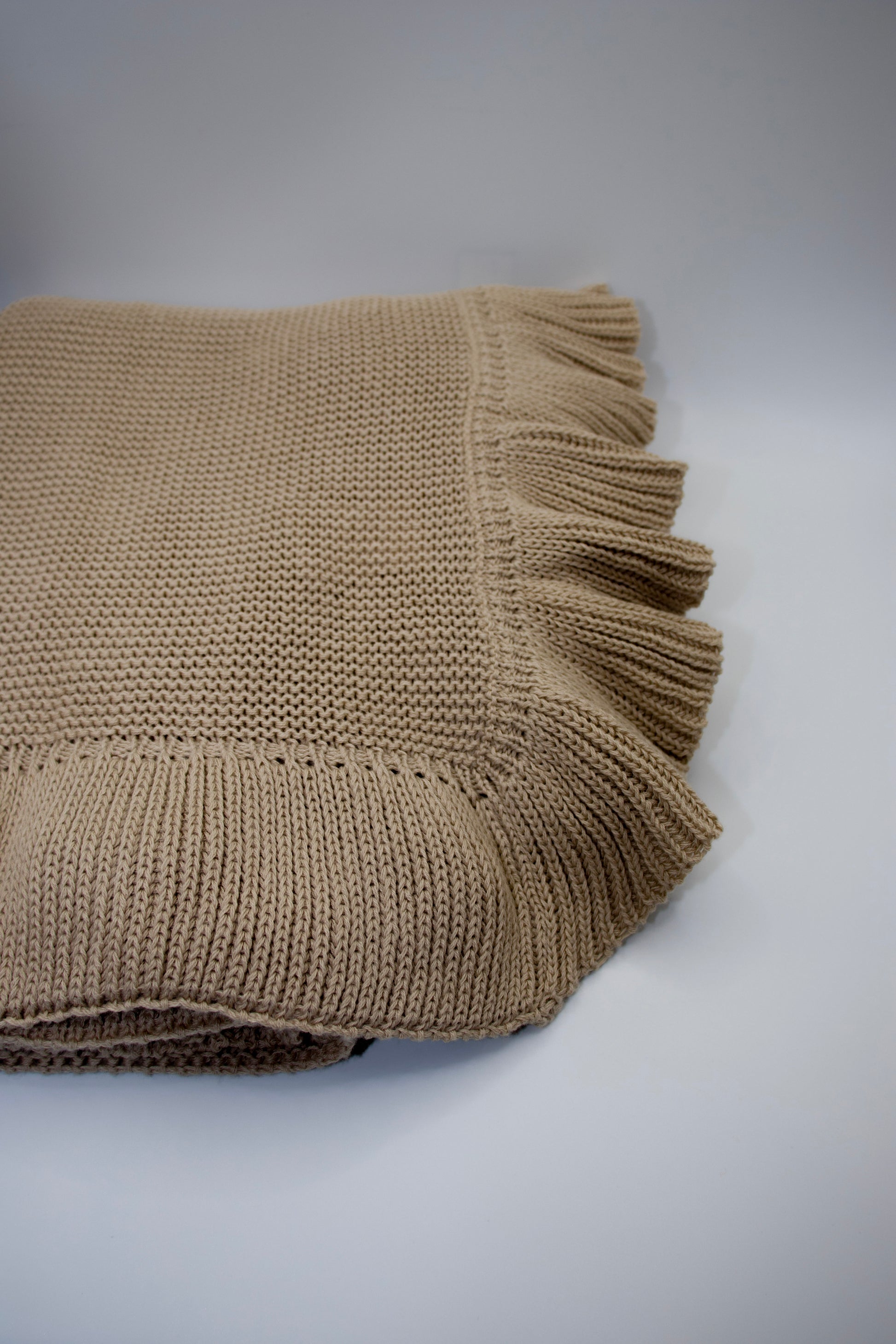 Beige knitted blanket with frayed edge on a white background