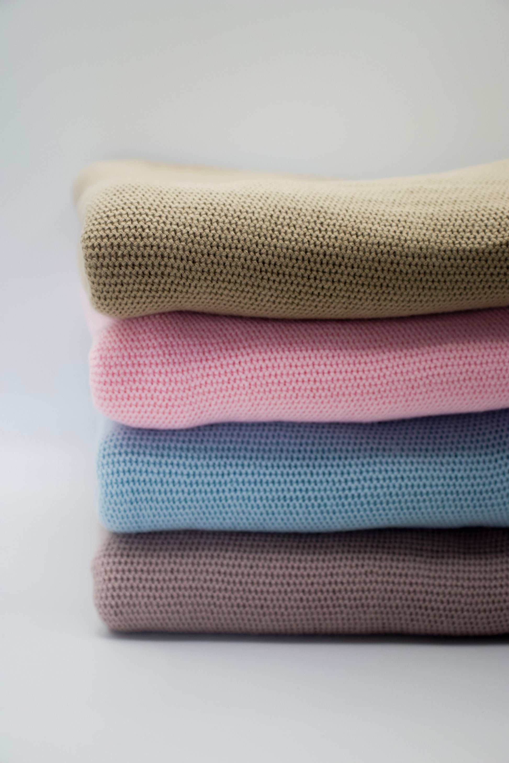 Stack of folded blankets in beige, pink, blue, and brown on a light gray background