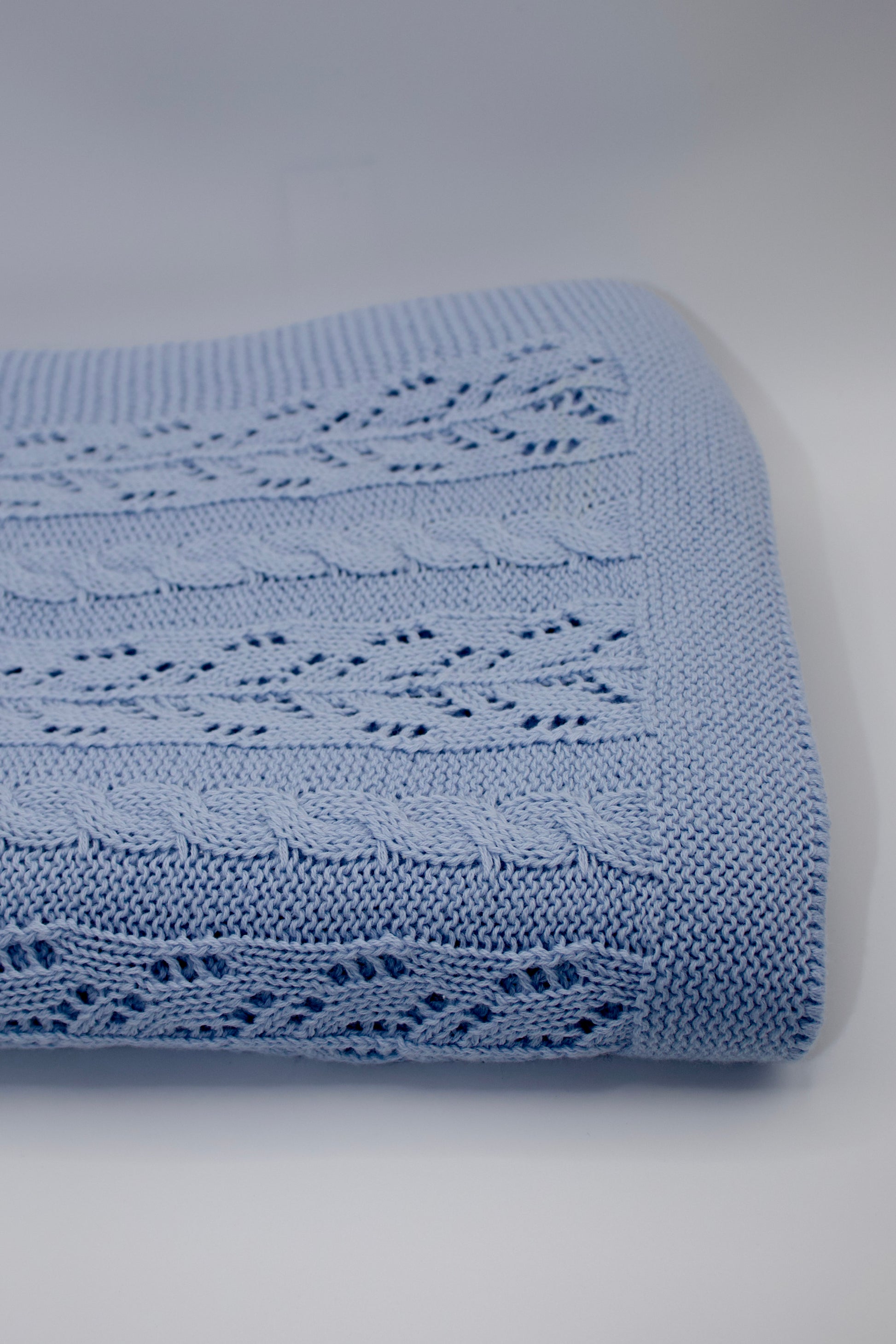 Blue knitted blanket with intricate patterns on a light gray background
