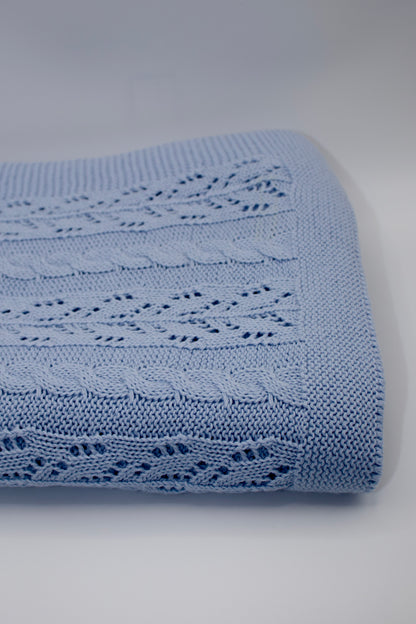 Blue knitted blanket with intricate patterns on a light gray background
